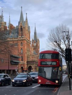 a red double decker bus driving down a street in front of tall buildings with towers