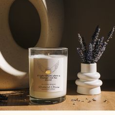 a white candle sitting on top of a table next to a vase filled with lavender