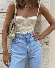 a woman standing against a wall wearing high waist jeans and a corset top