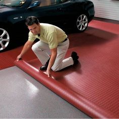 a man kneeling down on top of a red mat in front of a black car