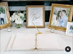 an open book sitting on top of a table next to two framed pictures and flowers