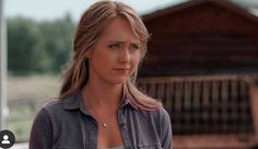 a woman standing in front of a barn looking off to the side with her hand on her hip