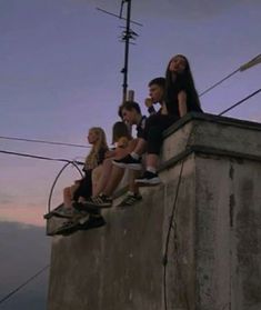 several people sitting on top of a cement wall next to power lines and telephone wires