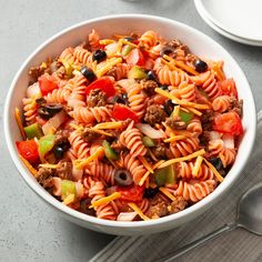 a white bowl filled with pasta salad next to silverware and utensils on a table