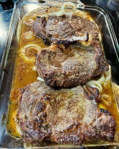 three steaks in a casserole dish with onions and gravy on the side