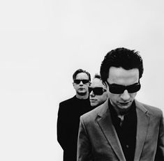 a group of men standing next to each other in front of a white wall with sunglasses on