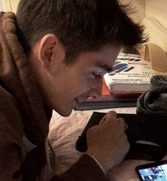 a man looking at his cell phone while laying on the bed with emoticions