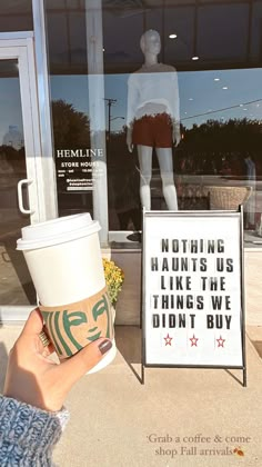 a person holding up a coffee cup in front of a mannequin