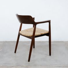 a chair with a woven seat pad on the back and armrests, sitting in front of a white wall