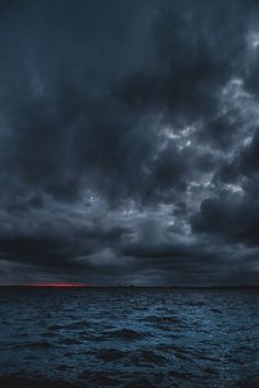 dark clouds over the ocean with red light in the distance and blue sky above it