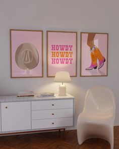 a white chair sitting next to a lamp on top of a wooden floor in front of two posters