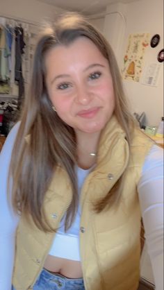 a girl with long hair wearing a yellow jacket and jeans is smiling at the camera