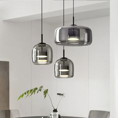 three lights hanging from the ceiling above a table with chairs and a vase on it