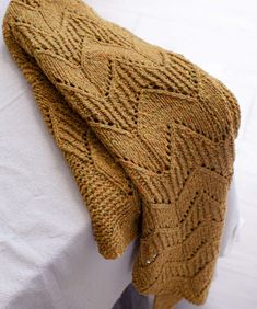 a brown knitted blanket sitting on top of a white bed next to a pillow