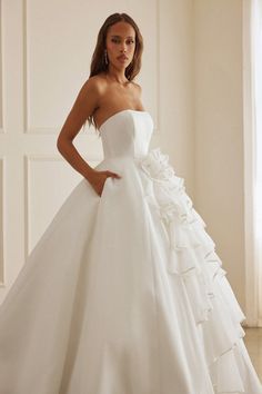 a woman wearing a white wedding dress with ruffles on the skirt and shoulder