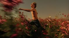 a young man standing in a field of flowers with his arms out to the side