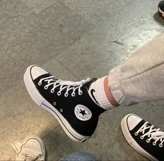 two people wearing black and white converse shoes