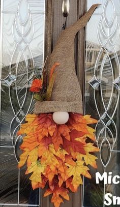 a scarecrow door hanger decorated with fall leaves and a burluck hat