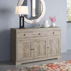 a wooden dresser with a mirror on top of it next to a lamp and rug