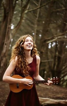 a woman in a red dress is playing an acoustic guitar and smiling at the camera