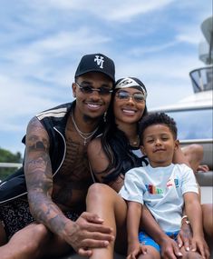 a man, woman and child sitting on the ground in front of a white boat