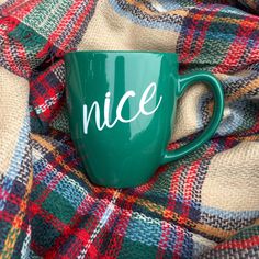 a green coffee mug with the word nice on it sitting on a plaid blanket,