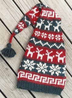 a red and black knitted hat with pom - poms on it sitting on a wooden surface