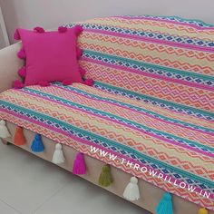 a couch covered in colorful blankets with tassels on the back and pink pillow