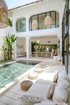 an outdoor living area with couches and pillows next to a swimming pool in front of a house