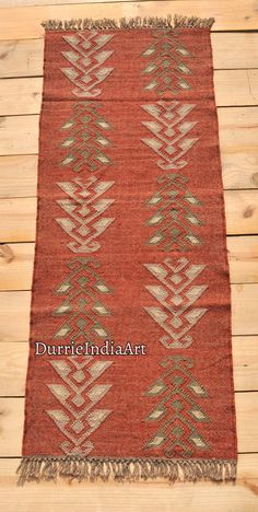 an old red rug with white and green designs on it, sitting on a wooden floor