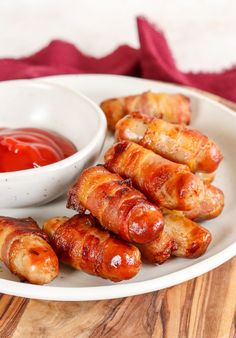 bacon wrapped hot dogs on a plate with ketchup and dipping sauce in a bowl