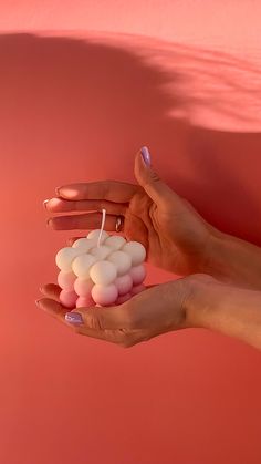 a person holding some small marshmallows in their hand against a pink background