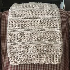 a white crocheted blanket sitting on top of a brown and white checkered couch