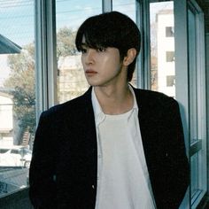 a young man standing in front of a window next to a glass wall and looking at the camera