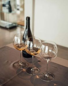 three wine glasses and a bottle on a table