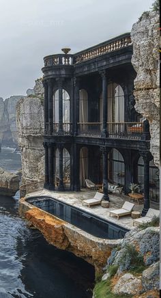 an old house with a pool in front of it near the water and cliffs on both sides