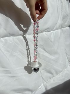 a hand holding a beaded necklace on a white sheet with pink and silver beads