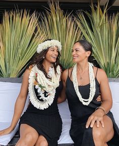 two beautiful women sitting next to each other on top of a white couch in front of palm trees