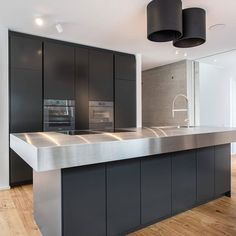 a modern kitchen with stainless steel counter tops and black cabinetry, along with wooden flooring