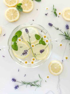 lemons, lavender and herbs in a glass cup on a white table with flowers