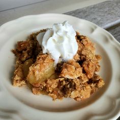 a white plate topped with an apple crisp and whipped cream topping on top of it