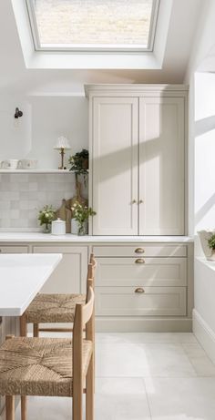 a white kitchen with skylight and wooden dining table in the center, surrounded by beige chairs