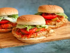 three chicken burgers with tomatoes and lettuce on a wooden cutting board, ready to be eaten