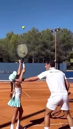 two people on a tennis court with rackets in their hands and one person reaching up to hit the ball