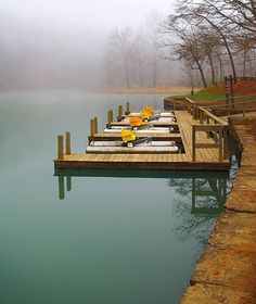 a dock with several boats tied to it in the foggy water near some trees