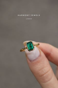 a woman's hand holding a ring with an emerald stone in the middle of it
