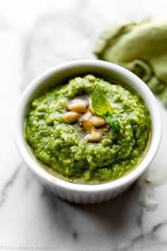 a white bowl filled with green pesto and topped with cashews on a marble surface