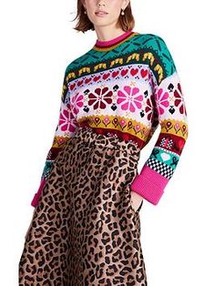 a woman is standing in front of a white background wearing leopard print pants and a colorful sweater