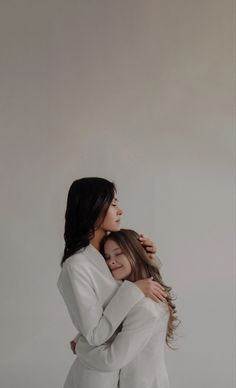 two women hugging each other in front of a white wall