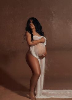 a pregnant woman in a white dress poses for the camera with her hands on her belly